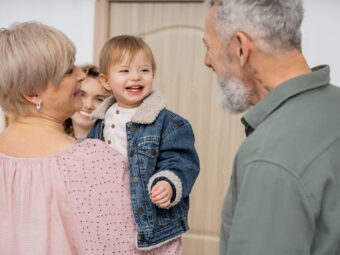 carefree child in denim jacket smiling near mother and happy grandparents in hall at home